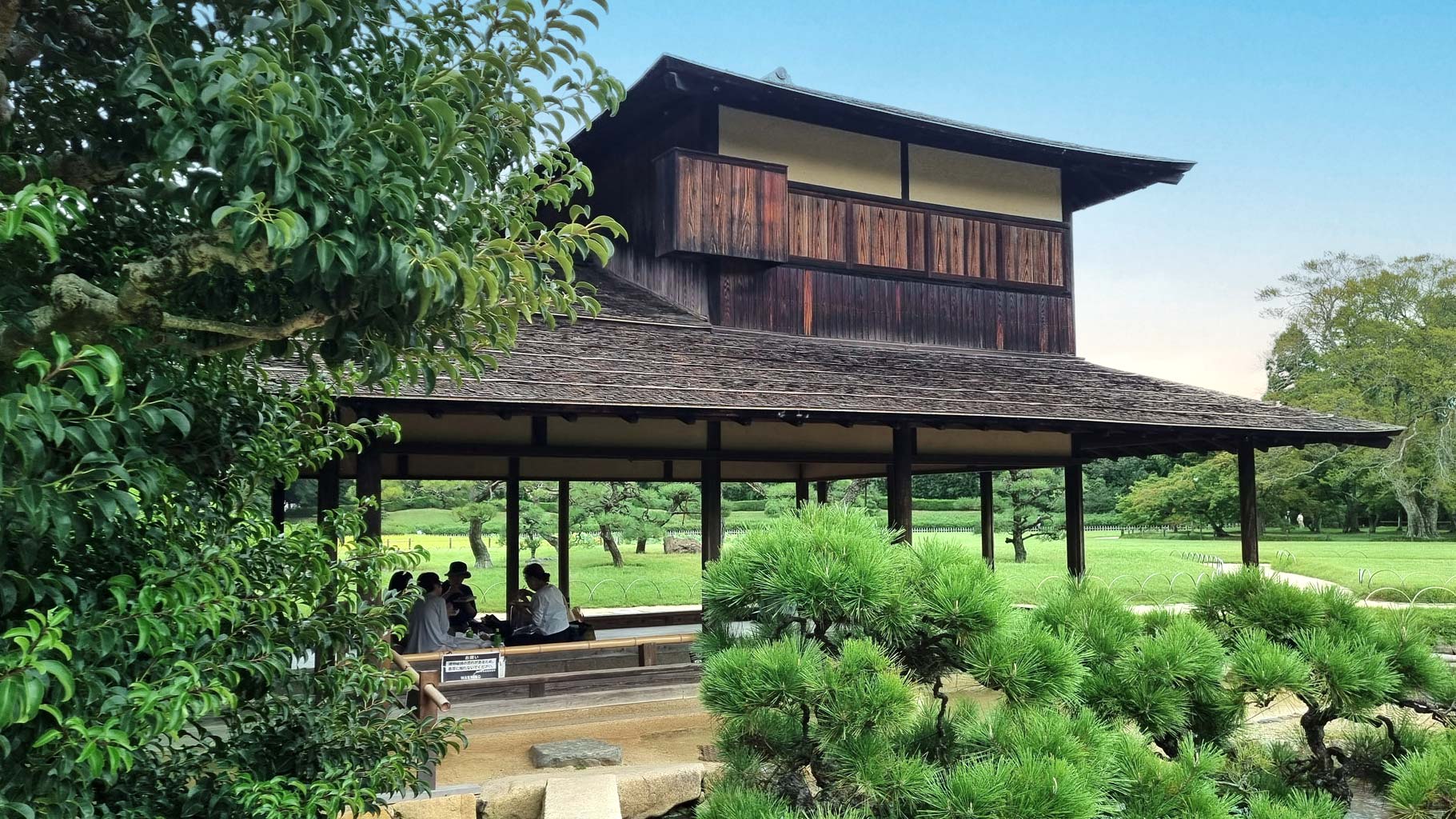 a traditional japanese tea house situation in a garden where you can see a few people seated in the background having lunch