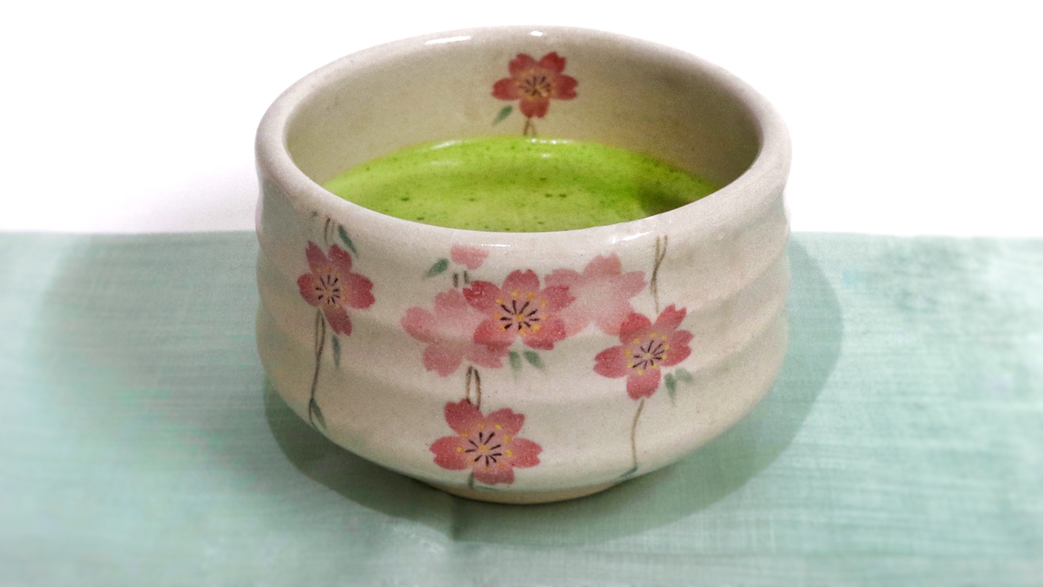 a japanese ceramic bowl, decorated with pink flowers, containing prepared matcha